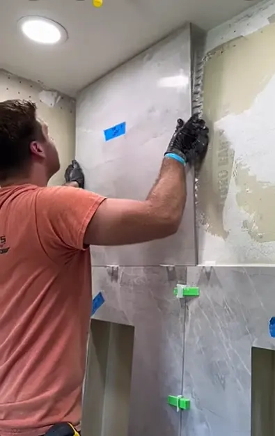 Tiler installing grey large format tiles with leveling clips in shower