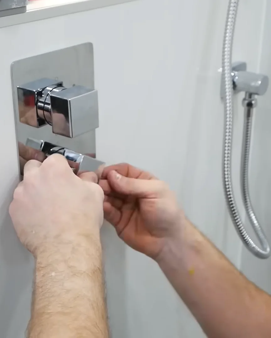 Hands installing or adjusting chrome shower controls inside walk-in shower wall