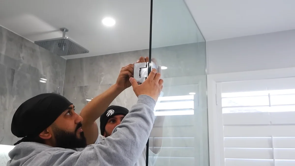 Technician mounting glass shower enclosure with metal hardware